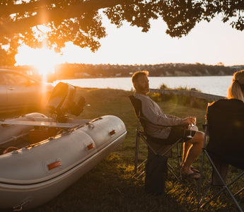 two people sitting in lawn chairs by the water with an inflatable boat