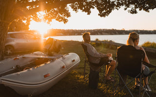 two people sitting in lawn chairs by the water with an inflatable boat
